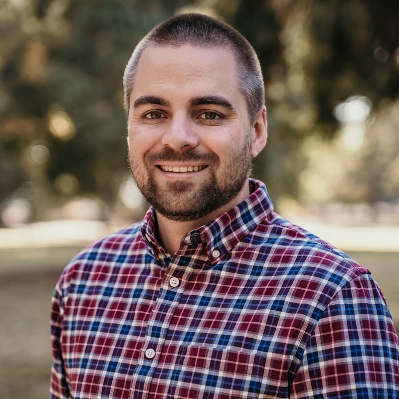 Headshot of Jake Richardson, smiling, in a plaid shirt outdoors