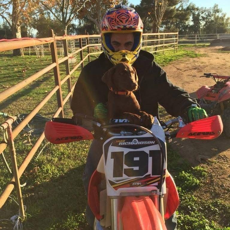 Jake sitting on a red dirt bike with a JAKE RICHARDSON 191 number plate, holding a chocolate lab puppy